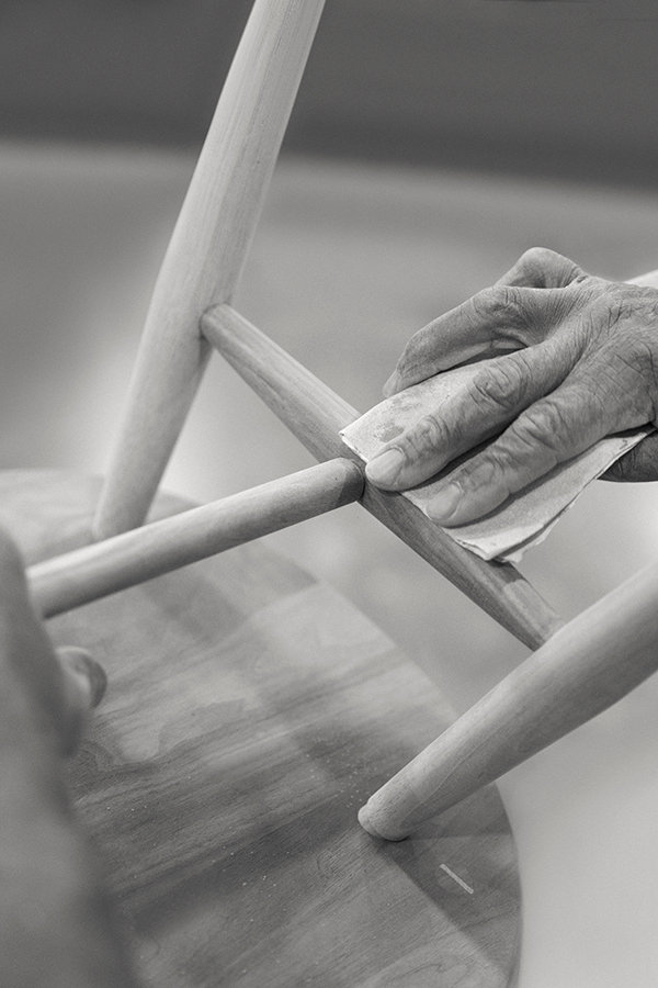 Greyscale image of a hand sanding the bottom of an ercol chair