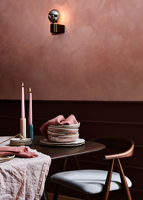 Tightly cropped shot of pink dishes and candles on a Corso table in front of a pink wall