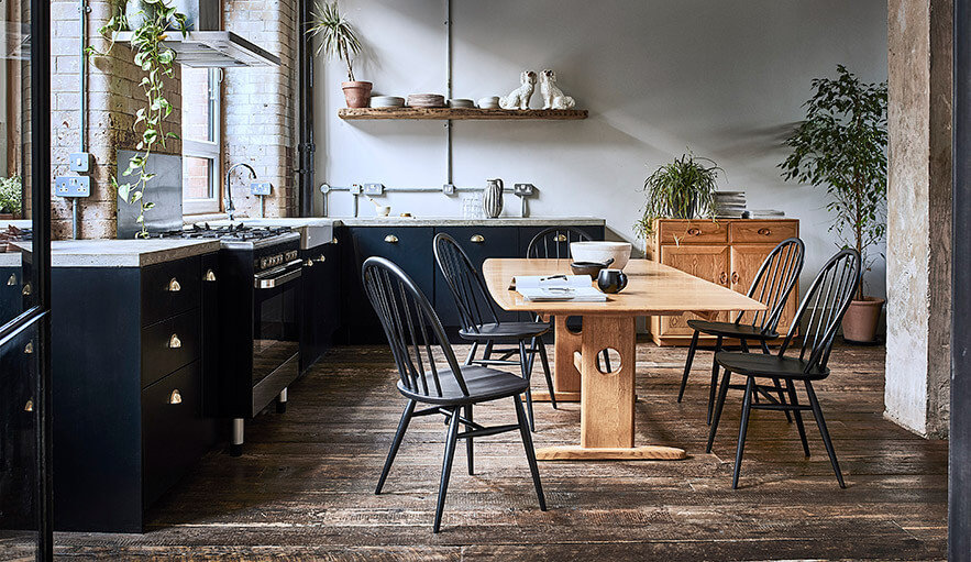 Black dining chairs at an oak Windsor dining table in a kitchen with dark cabinets