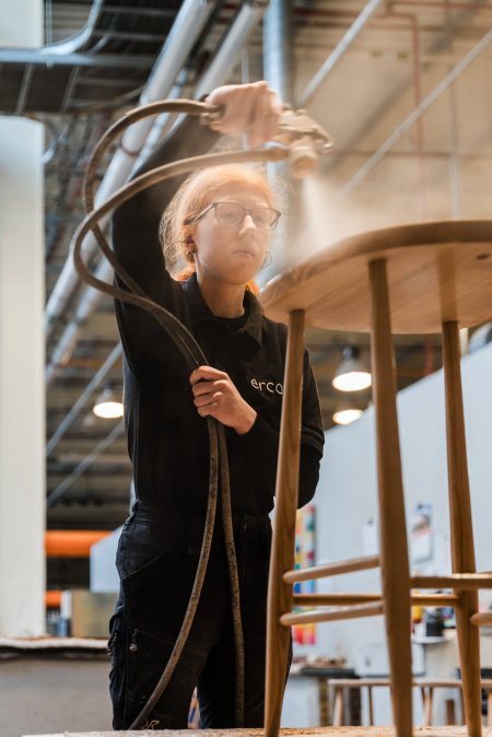 A polishing apprentice spraying an ercol wooden stool with wood stain