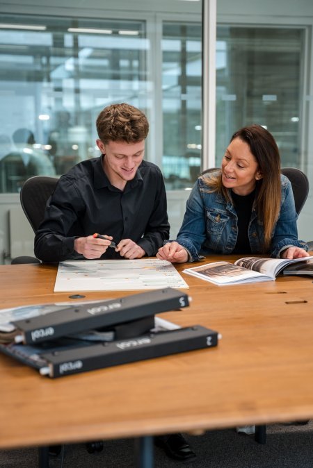 A young marketing apprentice sat at a large wooden table studying some papers with his mentor