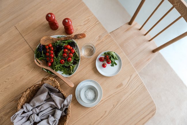 A top down view of an ercol dining table and chair, set with a tomato salad and salt and pepper grinders, showing the unique grain of the timber