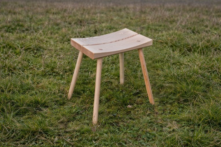 An ercol x Sylva Foundation curved stool, sat on grass